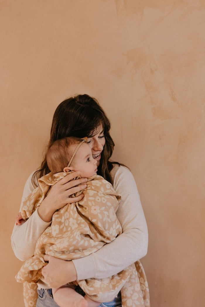 mommy hugging baby girl covered with the best baby wrap the meadow desert swaddle blanket