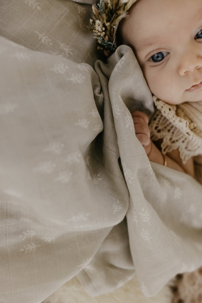 blue-eyed baby girl lying on top of the christmas swaddle which is the Forest in Gray Wolf color