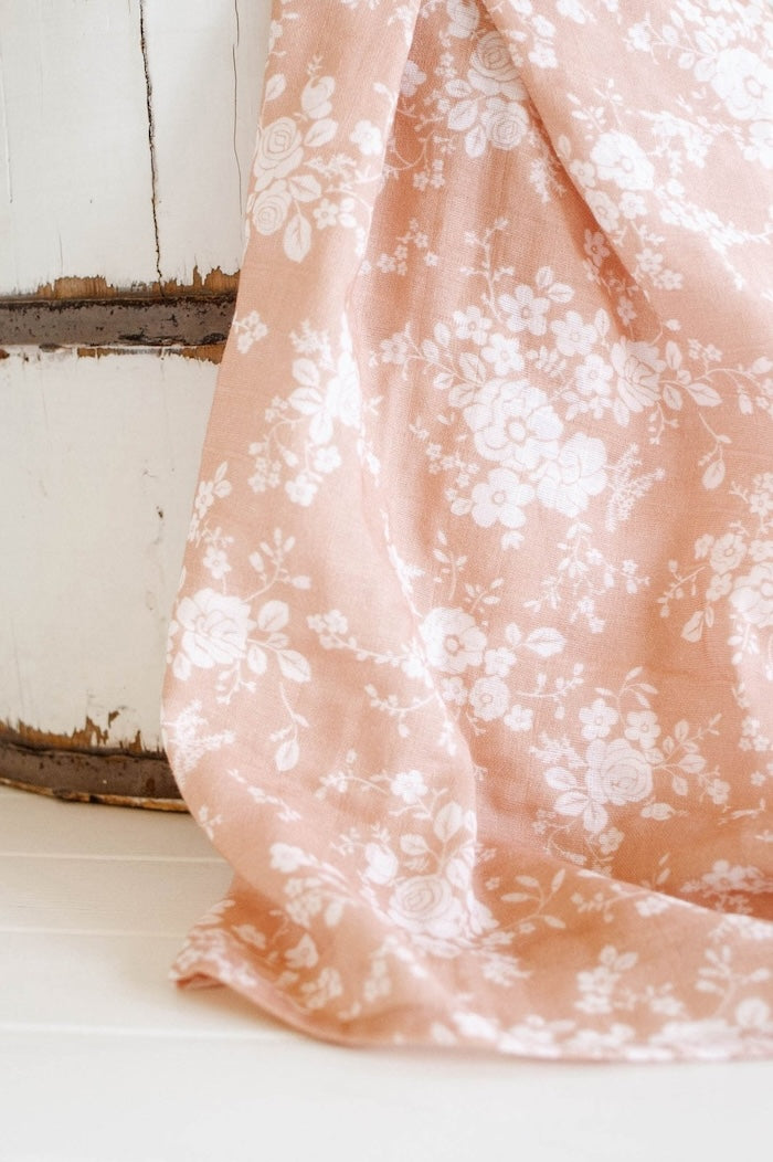 a close up photo of the newborn baby wrap in the vintage bouquet peach swaddle muslin blanket