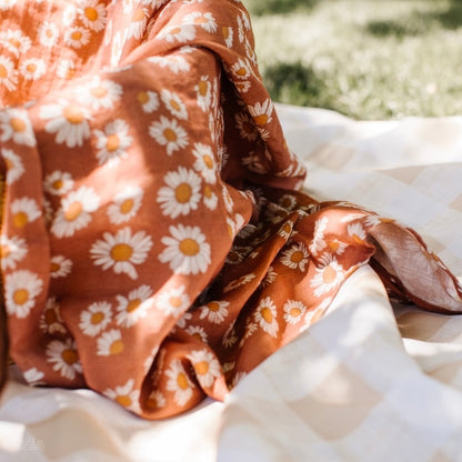 An earthy clay brown color with Daisy floral design swaddle laid down and loosely wrapped on a basket.