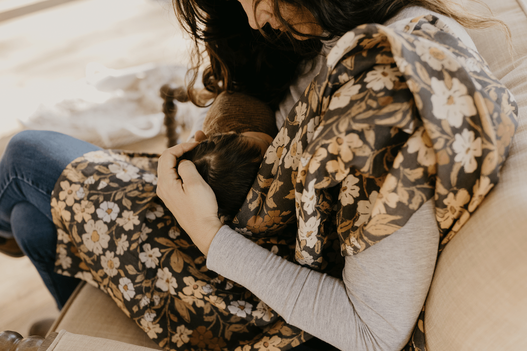 a photo of a mom breastfeeding her little baby in the couch using the flower swaddle as a nursing cover and nursing blanket