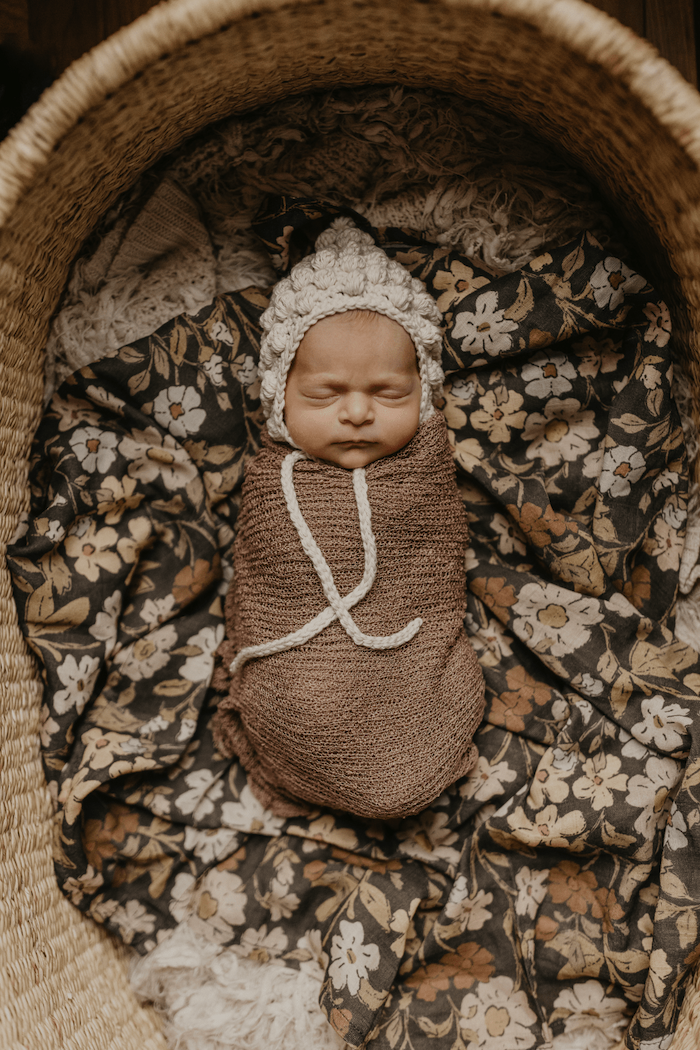 a beautiful photo of a swaddled baby sleeping soundly in a baby bassinet covered in our thicket flower swaddle that works perfectly in any newborn photo outfits