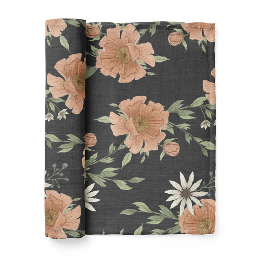 peony bloom swaddle blanket. pretty illustrations of a pink peony flower on a dark charcoal gray backdrop. The cotton blanket is rolled up.