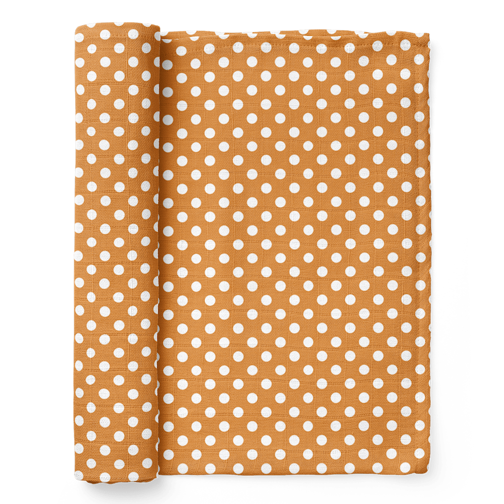 half rolled polka dot swaddle blanket in white dots over an amber color background