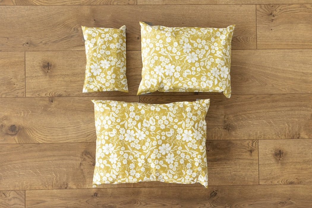 A photo comparing different sized poly mailers from Mini Wander. Mustard yellow color with white block printed flowers. Pictured are sizes 12x15.5 , 10x13 and 6x9 self sealing plastic envelopes