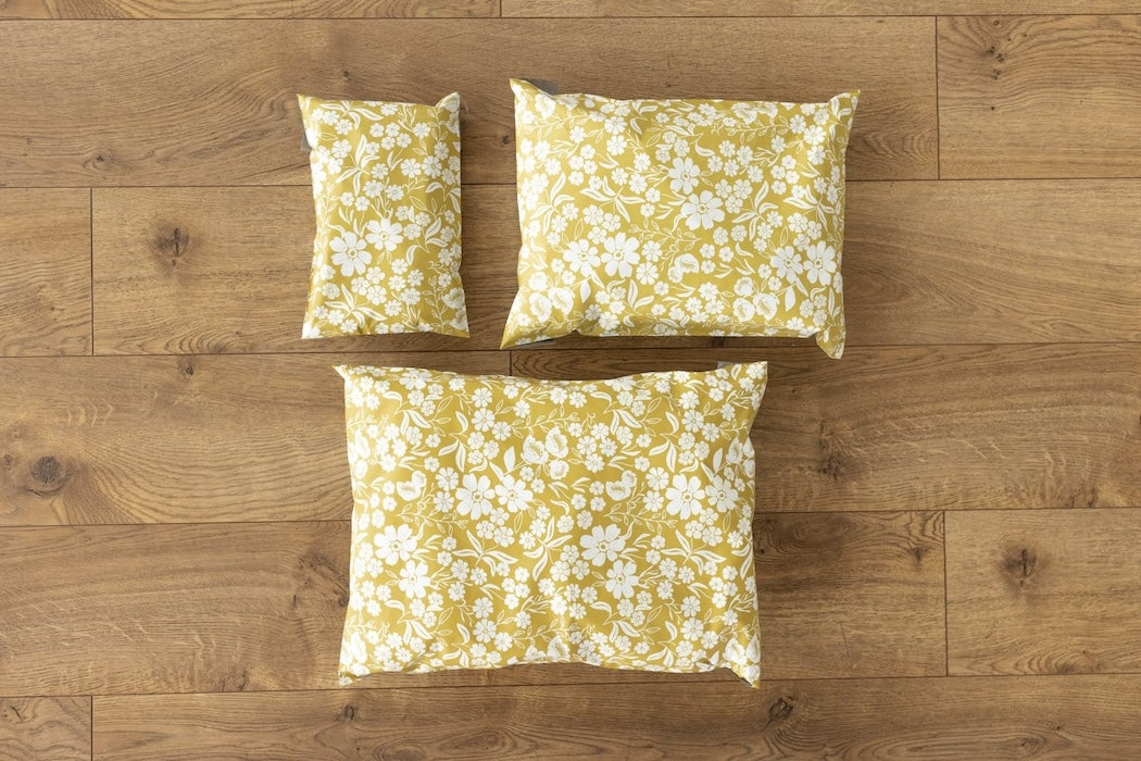 A photo comparing different sized poly mailers. Mustard yellow color with white block printed flowers. Pictured are sizes 12x15.5 , 10x13 and 6x9 self sealing plastic envelopes