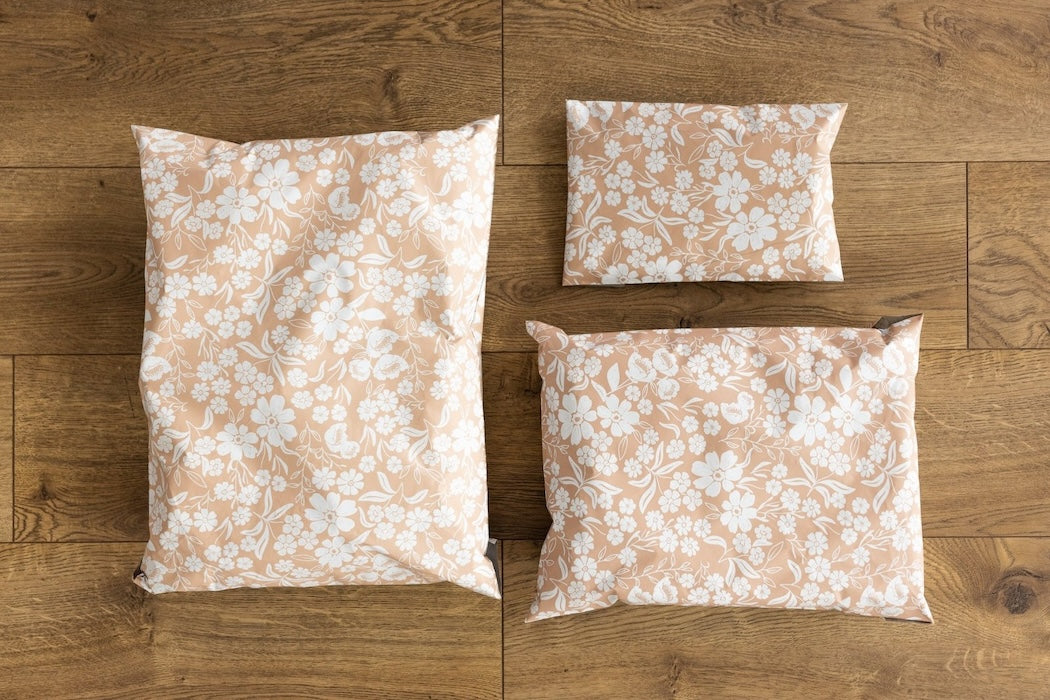 A photo comparing different sized shipping bags. Peachy pink color with white block printed flowers. Pictured are sizes 12x15.5 , 10x13 and 6x9 self sealing plastic envelopes