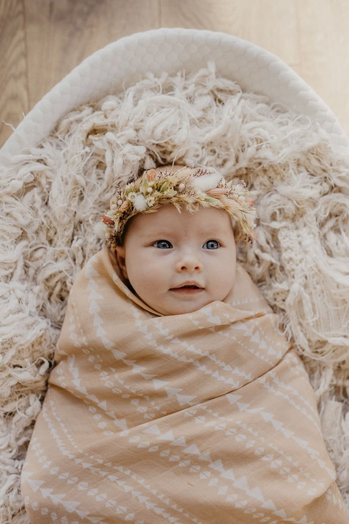 adorable baby girl wearing a flower crown lying in her white baby bassinet wrapped in our tribal receiving blanket