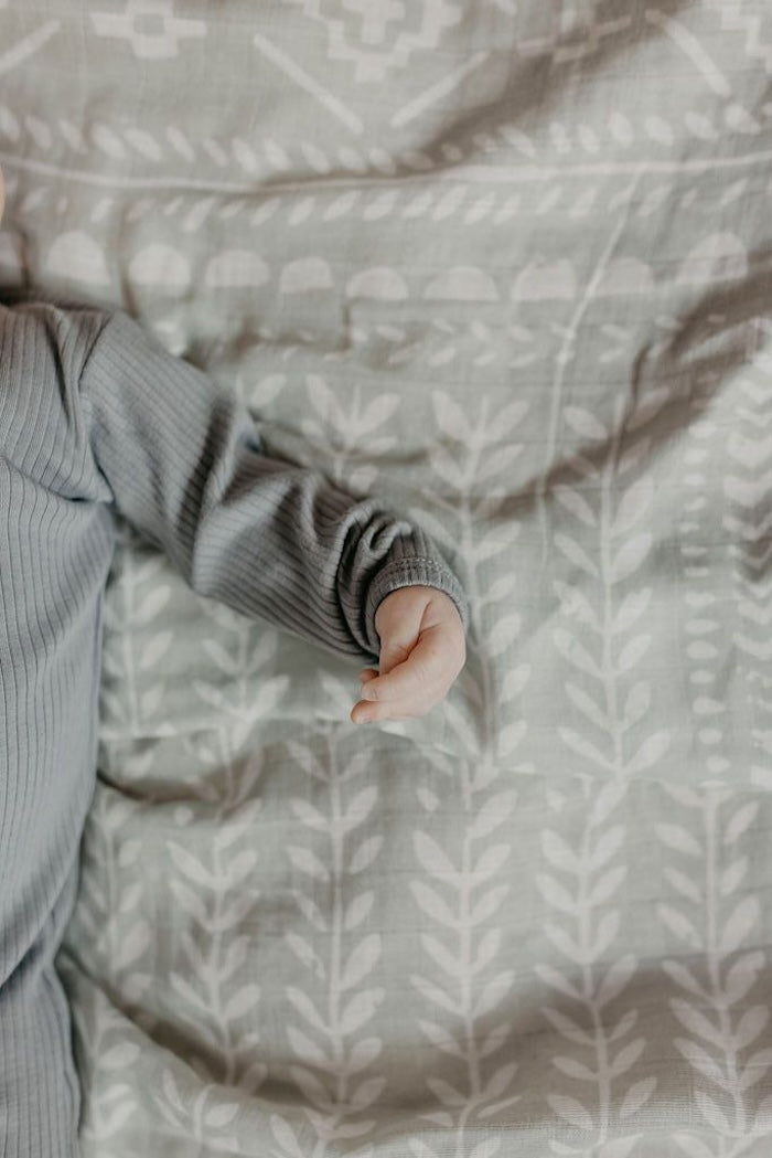 photo of a baby's arm and fist slightly clenched and fingers curled with our tapestry green spruce boy swaddle at the background