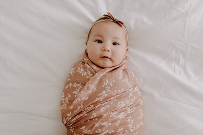 Baby smiling wearing a cute bow and wrapped in a mini wander bloom swaddle in sienna color