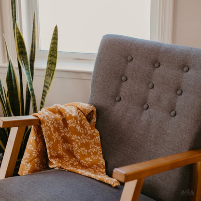 gray accent chair with the mustard leaf swaddle blanket draped on the right side armrest