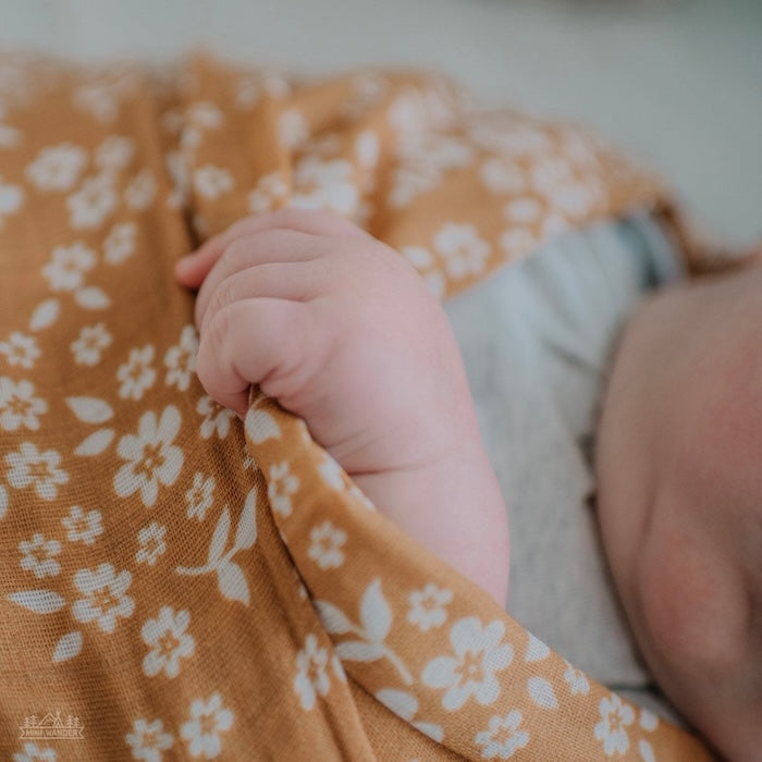 A close-up of a baby wrapped in a mustard swaddle with a whimsical floral design.