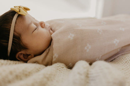 baby girl sleeping wearing a yellow leather bow headband wrapped in a pastel pink swaddle muslin
