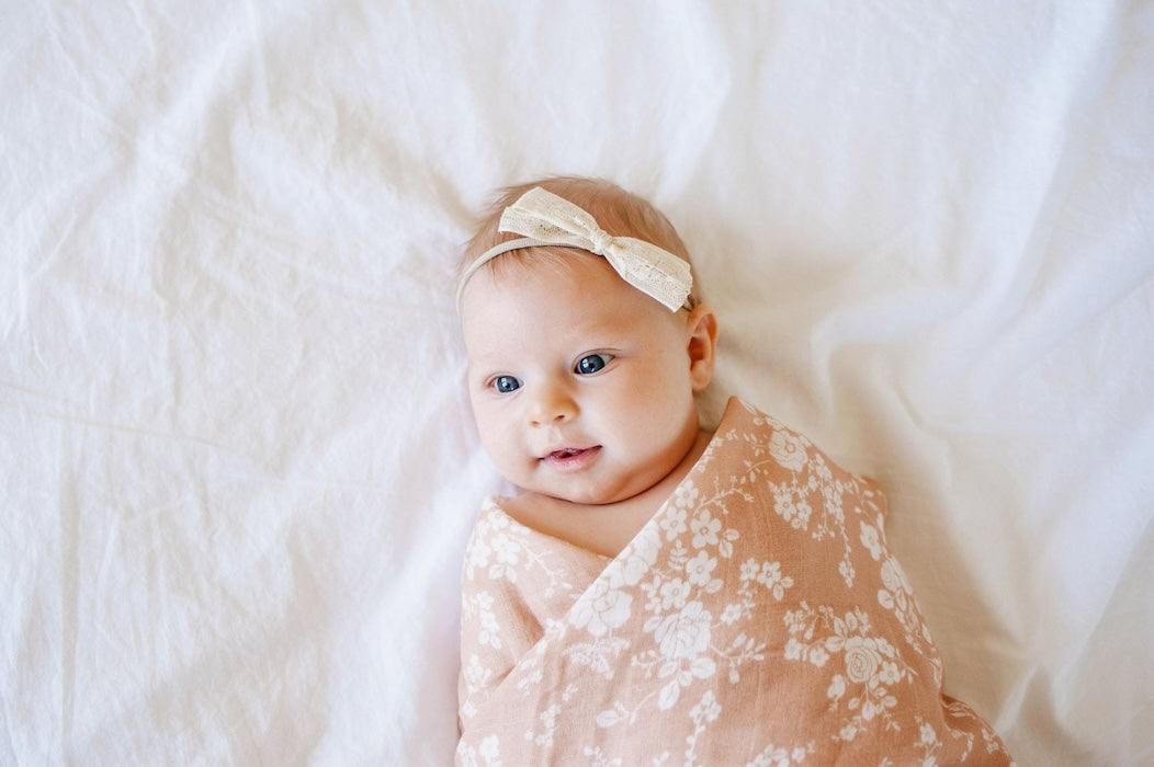 baby girl with a white lace headband wrapped in her vintage floral muslin swaddle in the color peach