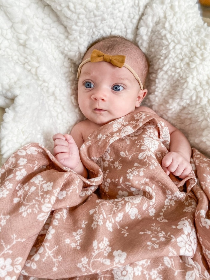 A baby wearing a brown bow is tucked into a Mini Wander swaddle with a vintage floral design.