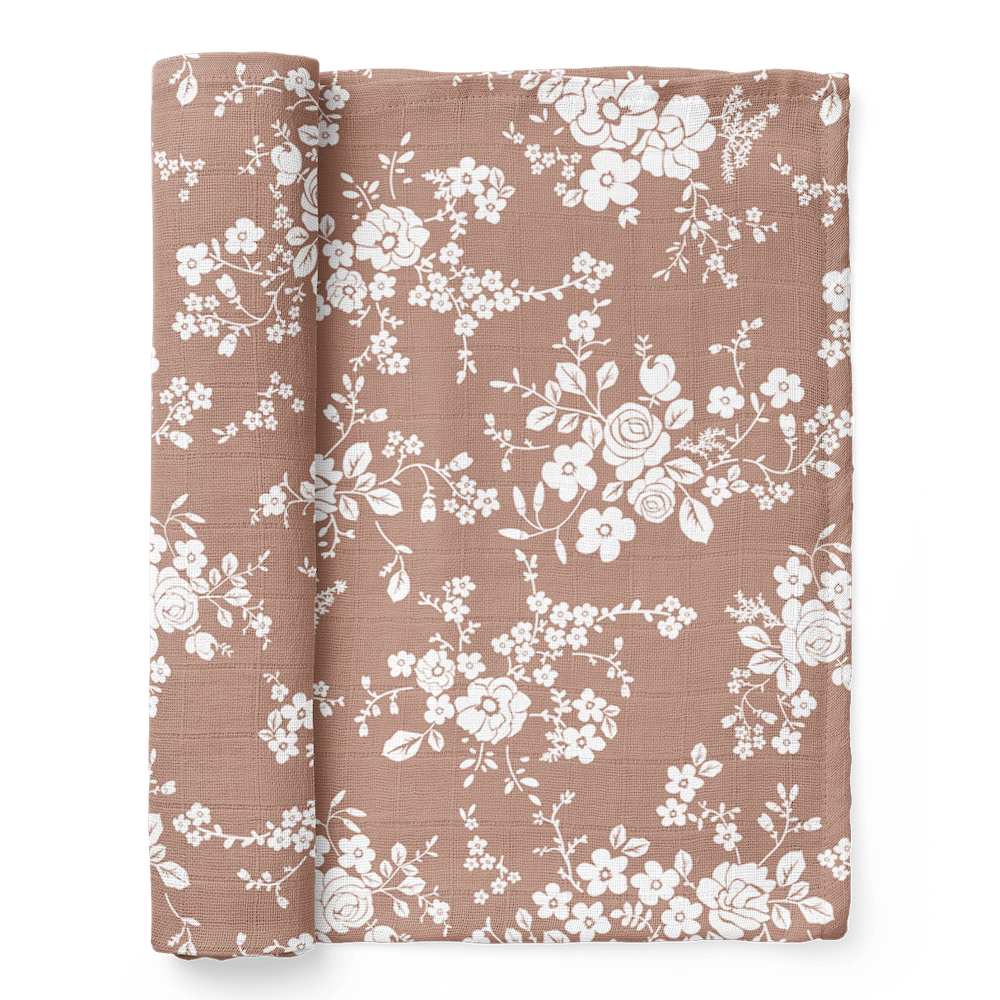 A half-rolled Mini Wander swaddle on a sienna background with vintage floral design