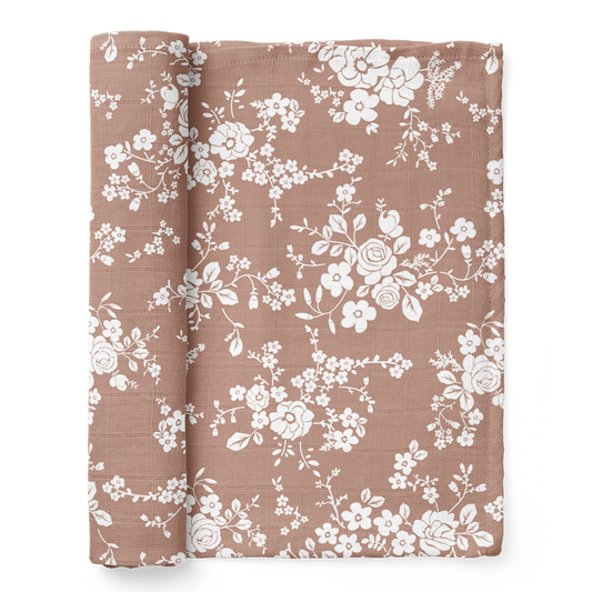A half-rolled Mini Wander swaddle on a sienna background with vintage floral design