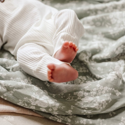 teeny tiny foot of a newborn baby wearing a white baby clothing lying on her soft and comfy vintage bouquet swaddle blanket in color green