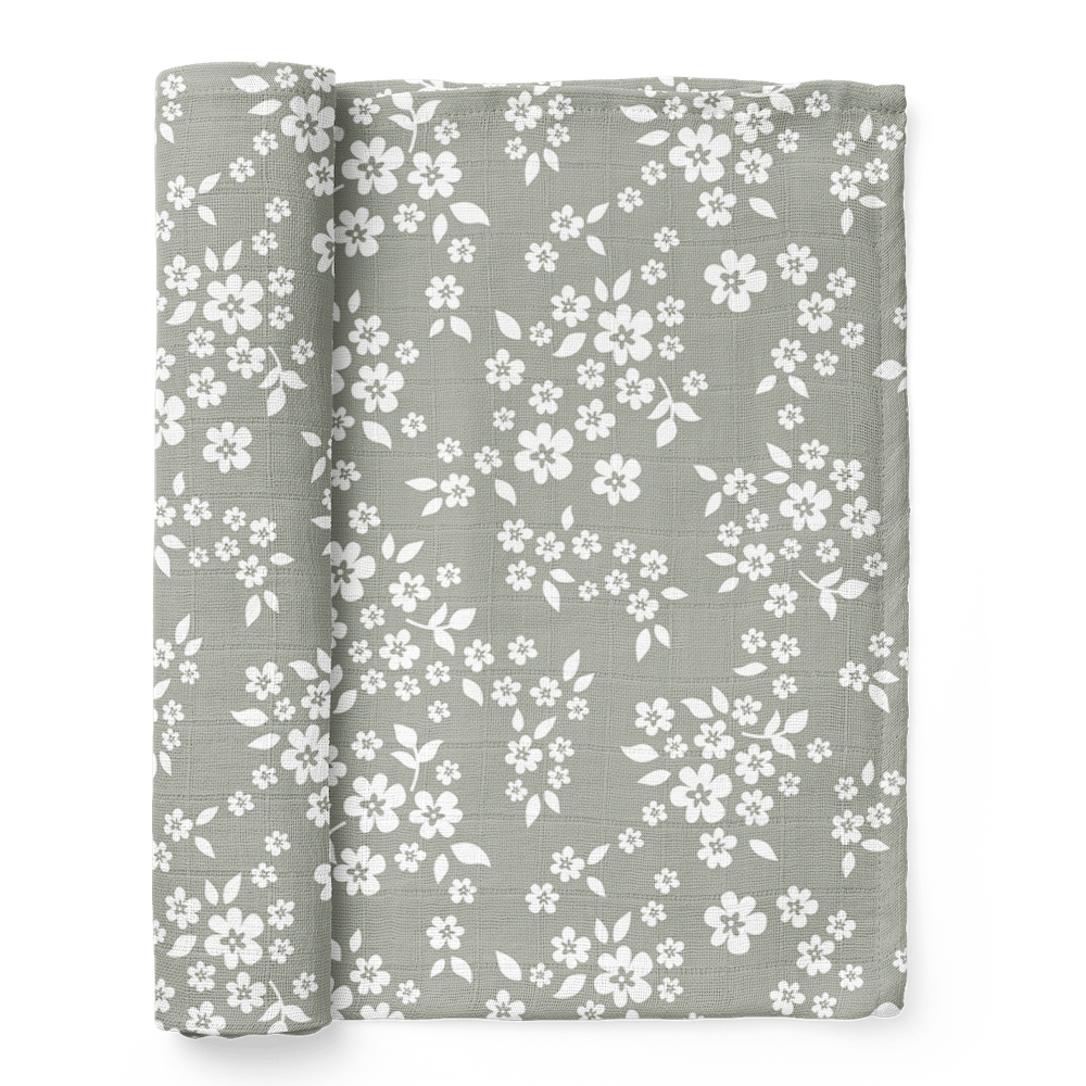 A half-rolled Mini Wander swaddle with a whimsical Floral design on a sage green background.