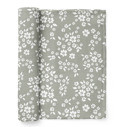 A half-rolled Mini Wander swaddle with a whimsical Floral design on a sage green background.