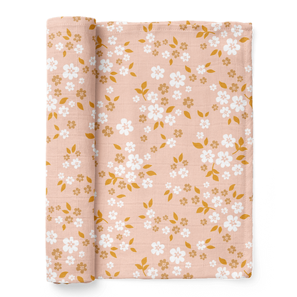 A half-rolled Mini Wander swaddle blanket peppered with daisies and delicate leaves design on a floral peach background.