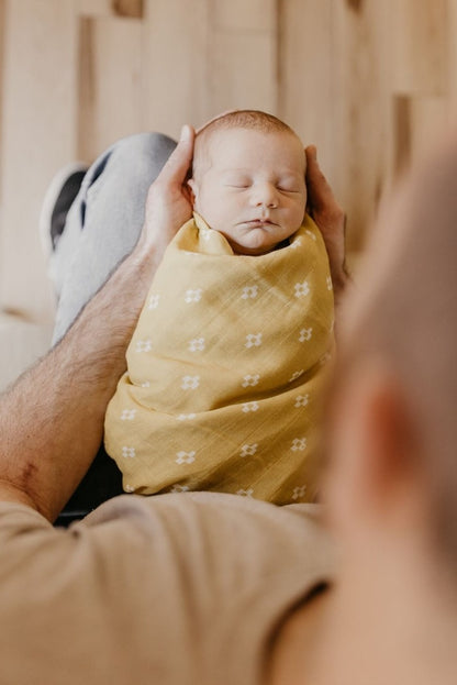 sweet sleeping baby held by his dad wrapped in the Boho Squares yellow baby blanket which is part of the baby gift set for boy