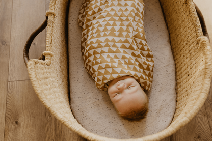 baby laid down on a baby bassinett sleeping sounddly and wrapped with our mountain swaddle in honey gold