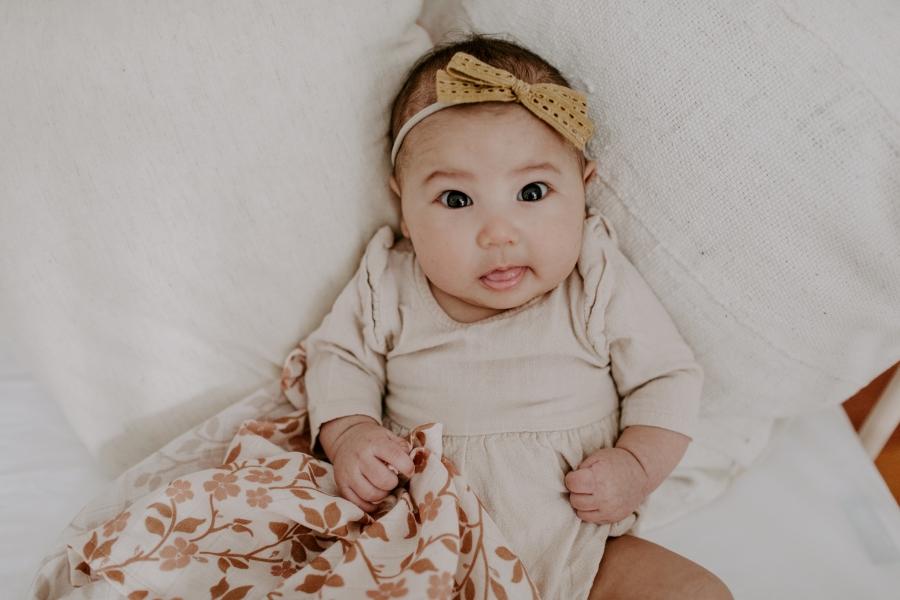 baby girl wearing a neutral colored clothes and mustard ribbon holding her baby blanket for baby girl in the magnolia tree brown design