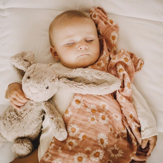 A baby sleeps with her bunny stuff toy wrapped in a pinkish floral swaddle.