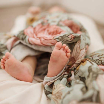 Baby is swaddled in Mini Wander sea foam garden floral, napping and showing off his adorable little feet.