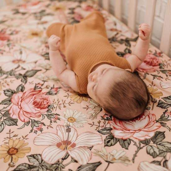 baby in a brown boho baby clothes lying on her crib lined with everyone's favorite nursery decor which is the Garden Floral pink crib sheets