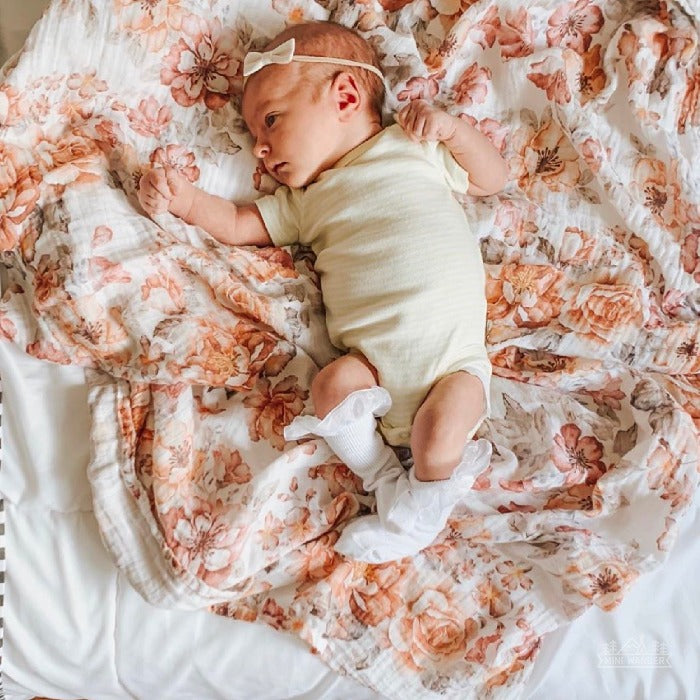 Baby is curled up on sunset garden floral from mini wander while dressed in creamy white onesies, a cute white bow, and lace socks. She had just awoken from an afternoon nap.