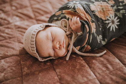 a sweet little baby sleeping wearing a knitted cap wrapped cozily in the spring blossom cotton swaddle