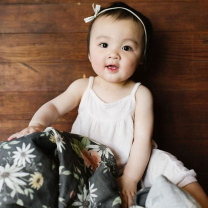 adorable baby girl wearing white headband and boho baby clothes smiling and looking at the camera with the spring blossom cotton swaddle in her lap