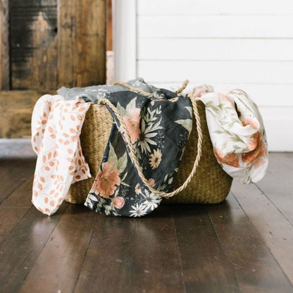 woven basket placed on the floor with three cotton swaddle tossed inside the blanket showing part of the three swaddles peeking outside the basket