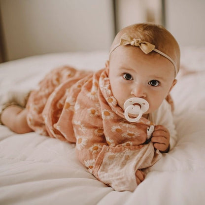A baby with a brown bow and a pacifier crawling in a Mini Wander pink flower design swaddle.