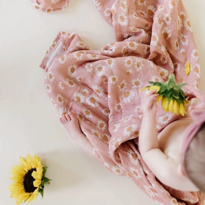 A baby playing with a sunflower while wrapped in a Mini Wander pink daisy swaddle.