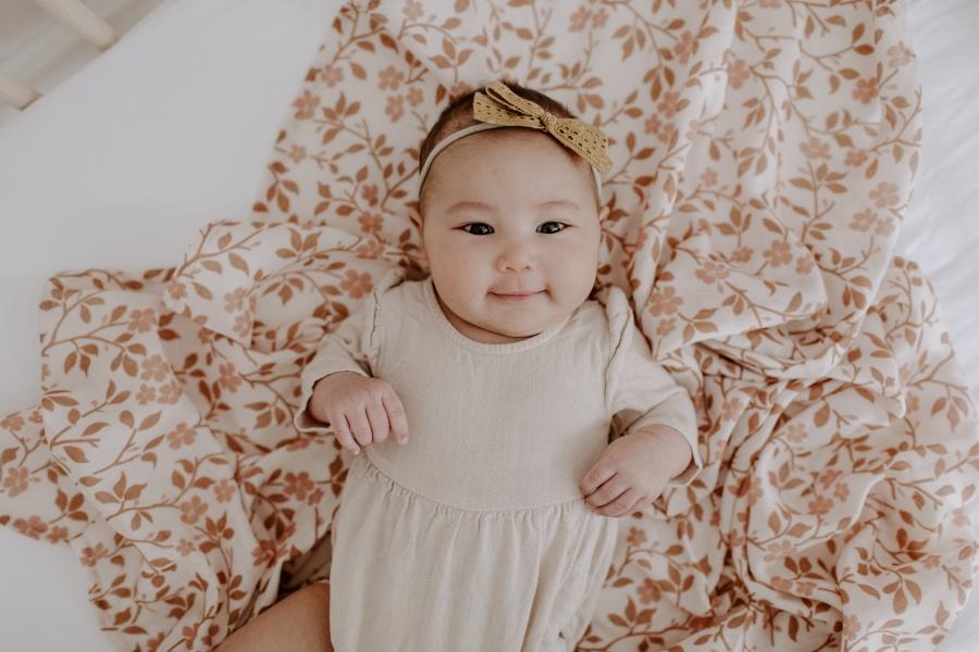 sweet and cuddly baby girl wearing a neutral toned baby clothes laying on her brown baby blanket in magnolia tree brown design