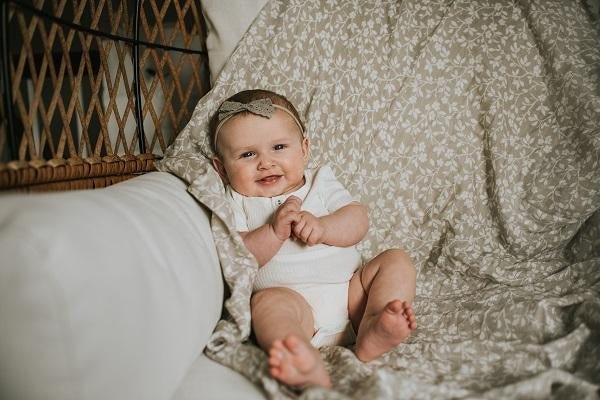 a cute baby girl wearing a white baby romper and gray headband leaning against her favorite floral gray baby blanket laid flat at the back used as a backdrop for photography