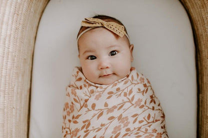 sweet baby girl laying on her baby bassinet wrapped in her muslin swaddle in the magnolia tree brown swaddle blanket 