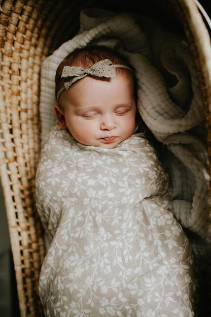a beautiful baby girl wrapped like a baby burrito using the floral gray baby blanket sleeping soundly inside her baby bassinet