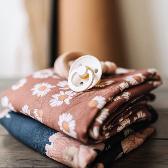 A Daisy floral design swaddle in an earthy clay brown color neatly folded on another Mini Wander Swaddle.