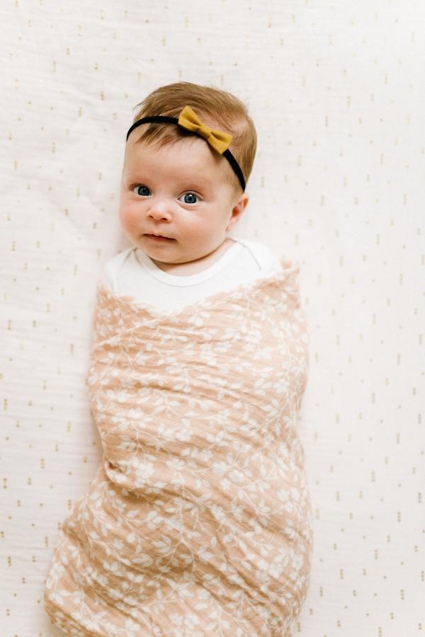 a sweet little girl wearing a bow headband wrapped in her floral pink swaddle blanket in the magnolia tree print pattern