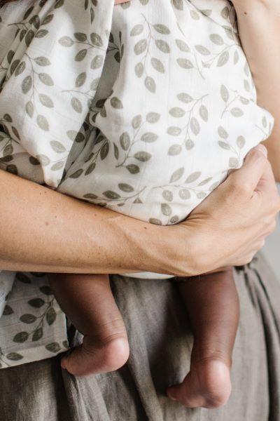 mom carrying baby only showing baby's feet wrapped in the classic leaves swaddle the perfect summer blanket for swaddling in the summer