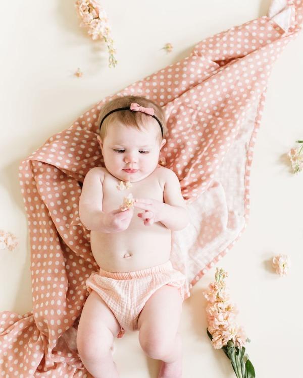 adorable baby girl laying on her back over the pink blush polka dot swaddle blanket