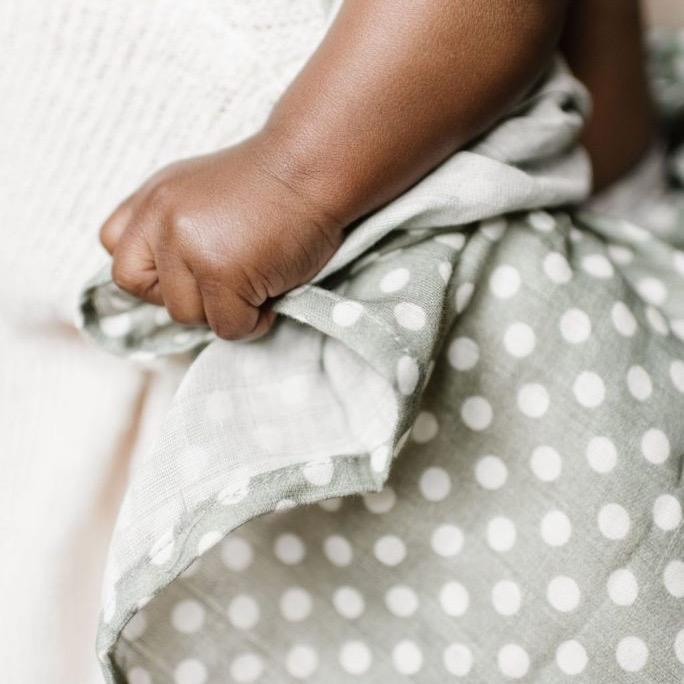 polka dot sage green swaddle blanket held by the little baby's tiny hands