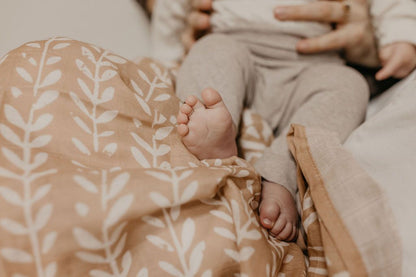 an image of a mom and baby focusing on the baby's little toes on top of our boho dusty pink swaddle 